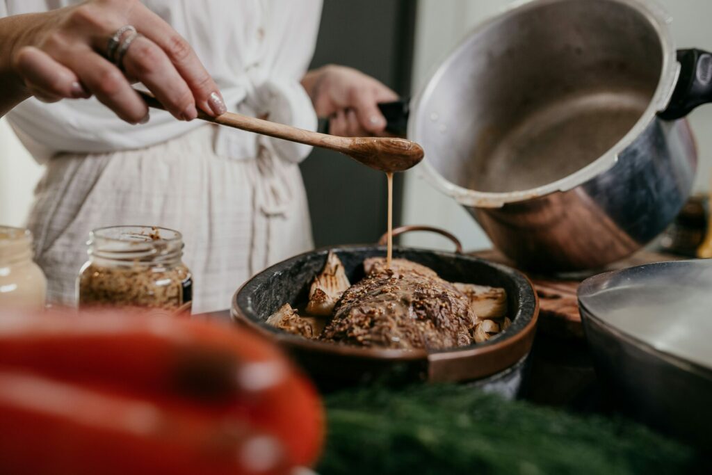 une femme qui verse de la sauce sur la viande dans un plat cuisine maison